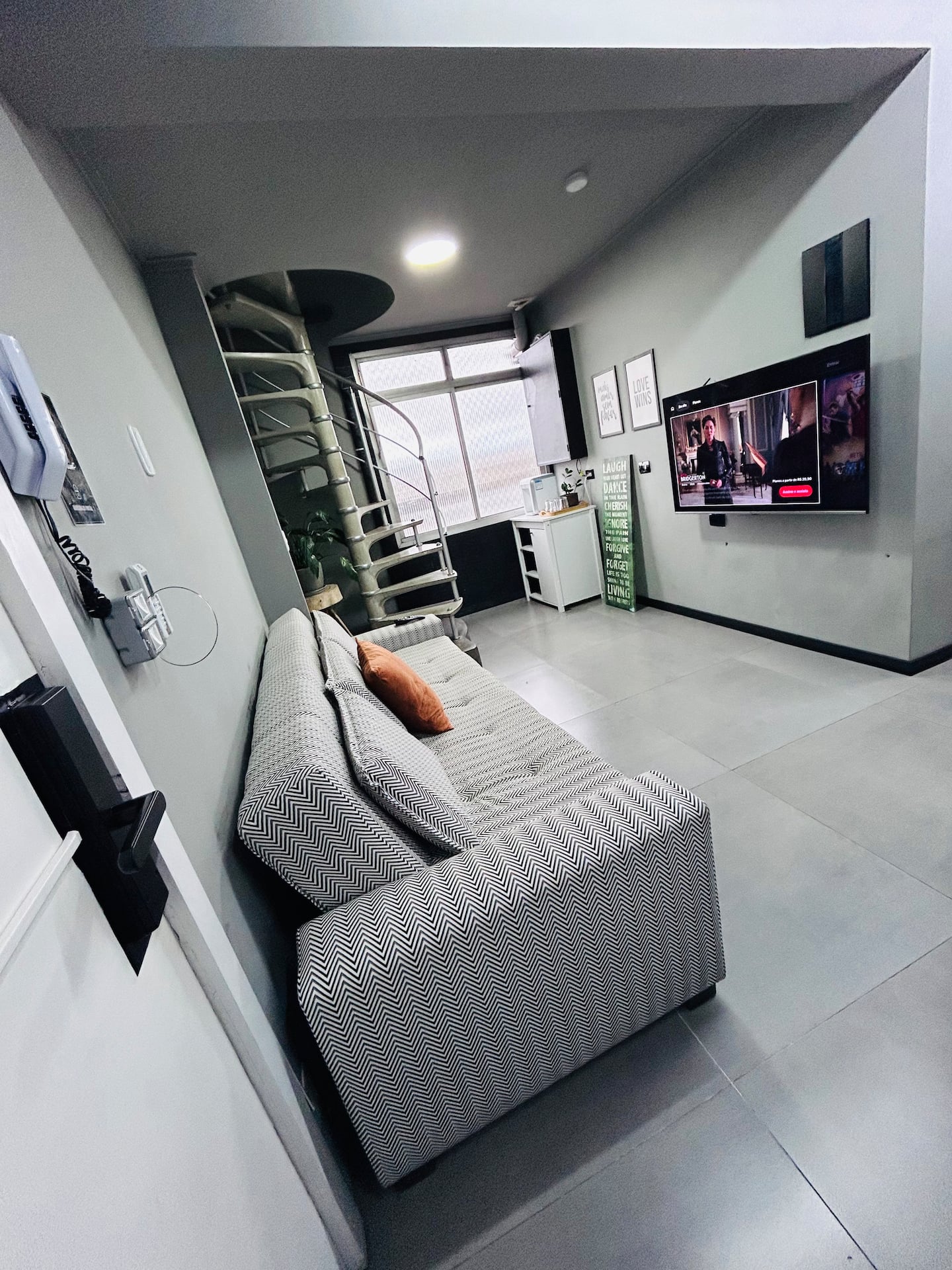 Sala com sofá, Smart TV e escada caracol para o mezanino