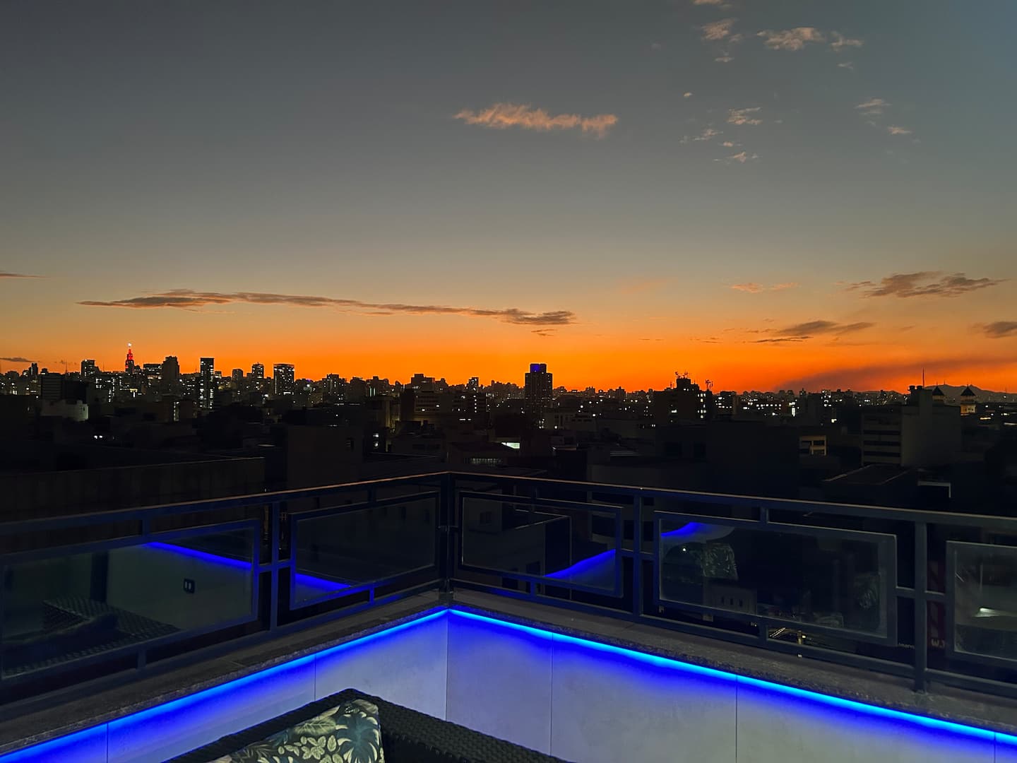Terraço à noite com iluminação em LED azul e skyline ao fundo